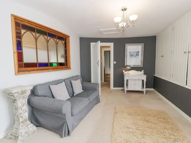 A room with a gray sofa and cushions a decorative pedestal a white cabinet with a lamp and artwork above built in cupboards on the wall and a beige rug on the floor at Capel Mawr in Llanrug near Llanberis