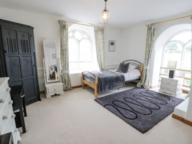 A bedroom with a single bed a full-length mirror a large black wardrobe and a gray rug at Capel Mawr in Llanrug near Llanberis