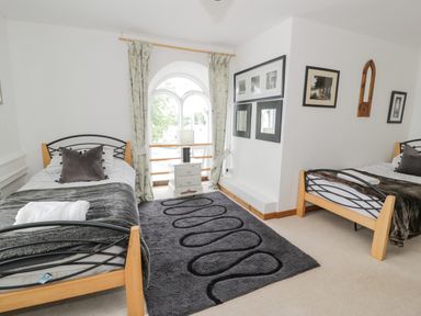 A bedroom with two beds a nightstand and lamp between them a dark rug on the floor and framed pictures on the wall at Capel Mawr in Llanrug near Llanberis