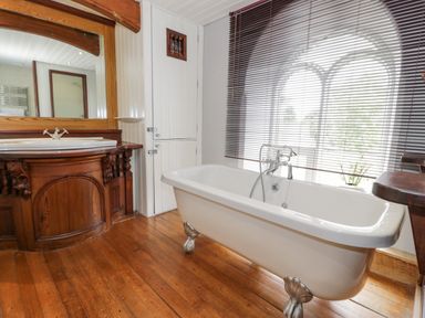 A bathroom with a clawfoot bathtub a wooden vanity with a sink and a large mirror and a window with blinds at Capel Mawr in Llanrug near Llanberis