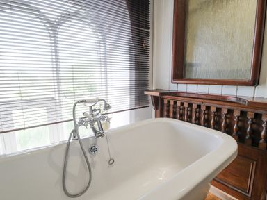 A bathroom with a white bathtub and a wooden cabinet with a mirror behind it at Capel Mawr in Llanrug near Llanberis
