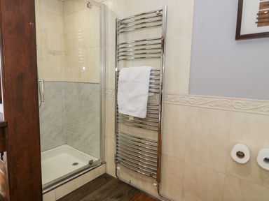 A bathroom shower with glass door and a chrome heated towel rail with towel at Capel Mawr in Llanrug near Llanberis