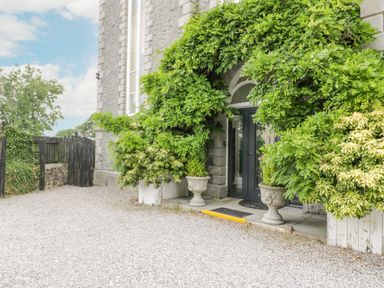 A stone building entrance with two potted plants and greenery around the door at Capel Mawr in Llanrug near Llanberis