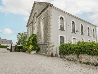Exterior view of a large stone and grey building with arched windows and greenery at Capel Mawr in Llanrug near Llanberis