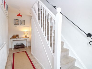 A hallway with a staircase and console table at Driftwood Cottage in Heacham