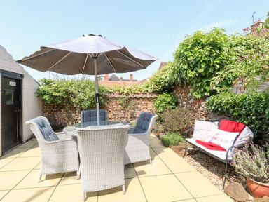 A garden with a table, chairs, and an umbrella at Driftwood Cottage in Heacham