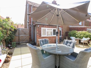 A garden area with a table and chairs under an umbrella at Driftwood Cottage in Heacham
