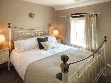 A bedroom with a metal bed frame bedside tables lamps and a window with curtains at Bwthyn Megan in Llangaffo near Newborough