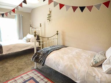 A bedroom with two single beds a hanging plant and a bunting decoration at Bwthyn Megan Llangaffo near Newborough