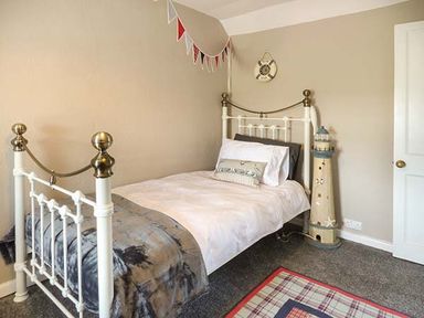 A bedroom with a single bed a lighthouse decoration a wall clock and a plaid rug at Bwthyn Megan Llangaffo near Newborough