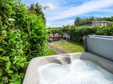 A backyard with a hot tub and outdoor seating area surrounded by hedges at Bwthyn Megan in Llangaffo near Newborough