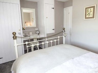 A bedroom with a white metal bed frame a desk with a chair a wall mirror and white doors at Bwthyn Megan in Llangaffo near Newborough