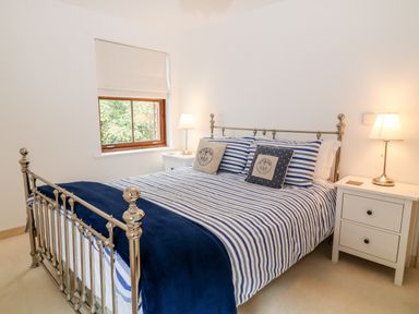 A bedroom with a metal bed frame striped bedding two side tables with lamps and a window with a roman blind at The Creekside in Looe