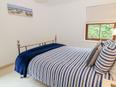 A bedroom with a metal bed frame a striped blue and white bedspread pillows a window and a wall painting at The Creekside in Looe