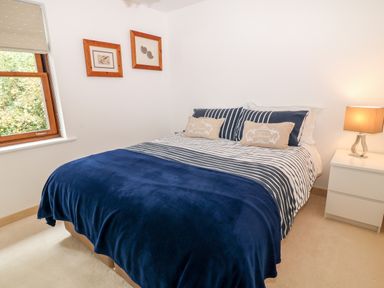 A bedroom with a double bed striped bedding pillows bedside table with lamp and two framed pictures on the wall at The Creekside in Looe