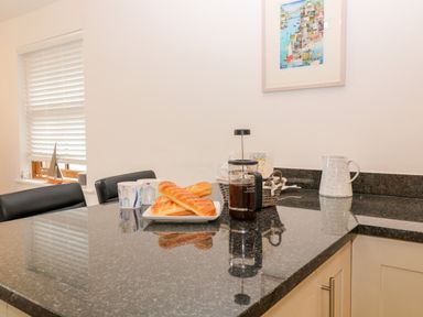 A kitchen countertop with a plate of bread a French press coffee maker mugs a pitcher and a basket at The Creekside in Looe
