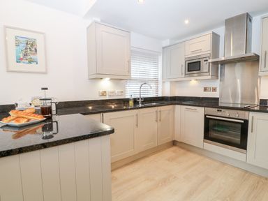 A kitchen with grey cabinets black countertops and bread on a plate at The Creekside in Looe