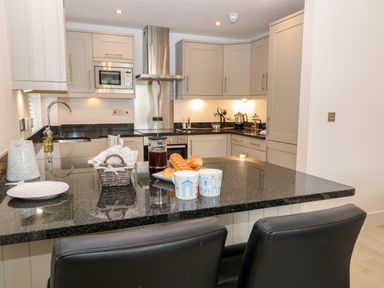 A kitchen with black countertop, two chairs, microwave, oven, kettle, and mugs on the counter at The Creekside in Looe