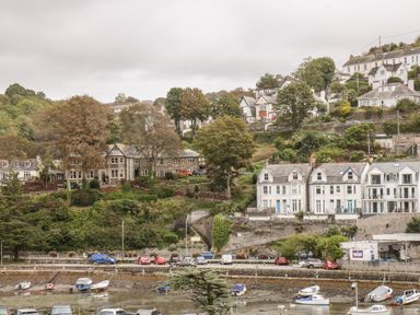 Boats moored near a shoreline with parked cars and houses on a hillside at The Creekside in Looe
