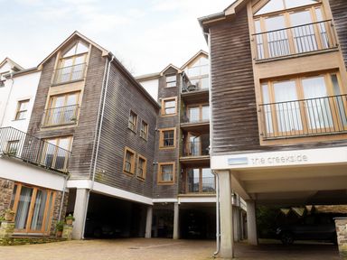 The exterior of a multi-story residential building with wooden siding balconies and covered parking at The Creekside in Looe