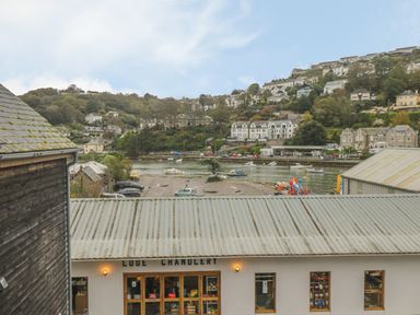 A building labeled Looe Chandlery with a view of boats on water and houses on hills in the background at The Creekside in Looe