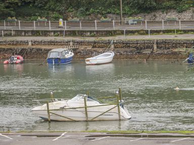A small motorboat in water secured with wooden posts and several other boats floating near a stone embankment