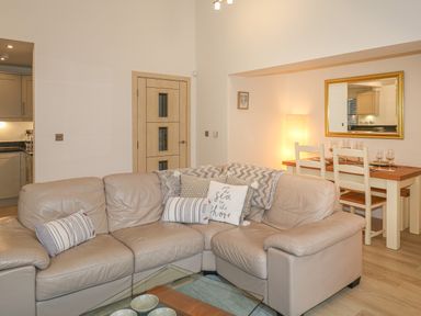 A living room with a beige leather sofa and a dining table with chairs and a mirror on the wall at The Creekside in Looe