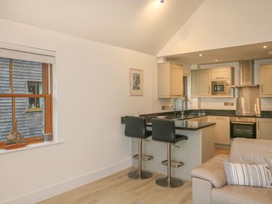 A kitchen with an island and two bar stools next to a beige sofa with a striped cushion at The Creekside in Looe