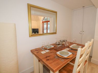 A dining table set with plates wine glasses and candles next to a mirror and two chairs at The Creekside in Looe