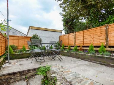 An outdoor patio area with metal chairs and table surrounded by wooden fencing and plants at 13 Castle Hill in Lostwithiel