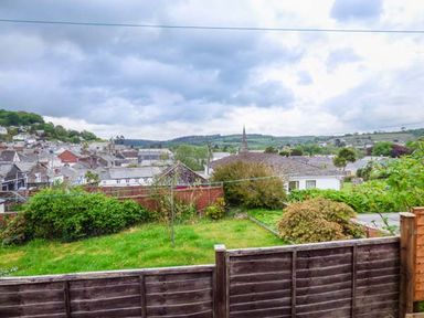 A backyard garden with grass and bushes overlooking houses and hills at 13 Castle Hill in Lostwithiel