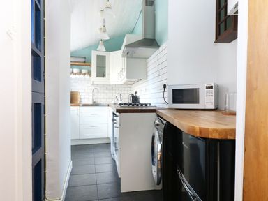 A small kitchen with white cabinets a wooden countertop a microwave a stove a washing machine and a sink at 13 Castle Hill in Lostwithiel