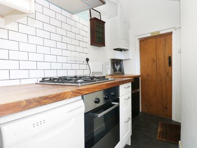 A kitchen with a wooden countertop gas stove oven dishwasher white tiled wall and wooden door at 13 Castle Hill in Lostwithiel