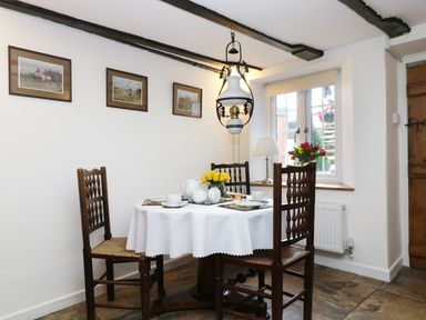 A dining area with a round table set for tea four chairs and framed pictures on the wall at 13 Castle Hill in Lostwithiel