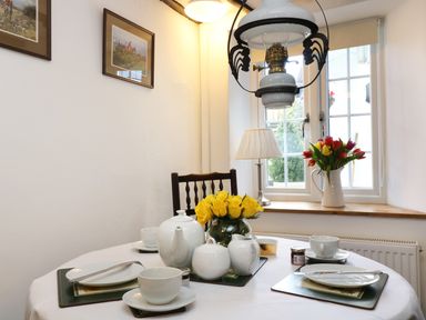 A dining table set with white tea service and yellow roses near a window with a vase of tulips at 13 Castle Hill in Lostwithiel