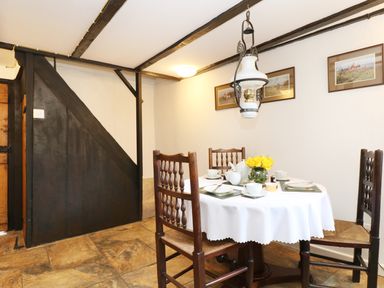 A dining area with a round table set for tea four wooden chairs and framed pictures on the wall at 13 Castle Hill in Lostwithiel