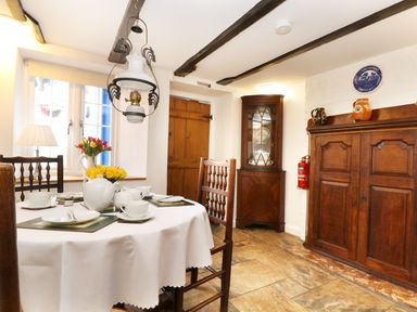 A dining room with a round table set for tea wooden chairs wooden cabinets and exposed ceiling beams at 13 Castle Hill in Lostwithiel