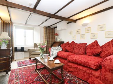 A living room with a red sofa, a wooden coffee table, a striped armchair, and framed pictures on the wall at 13 Castle Hill in Lostwithiel