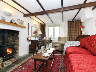 A living room with a red sofa, armchair, wooden coffee table, fireplace, and patterned rug at 13 Castle Hill in Lostwithiel