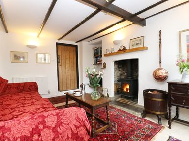 A living room with a red sofa a wooden coffee table flowers on table a fireplace and wooden door at 13 Castle Hill in Lostwithiel