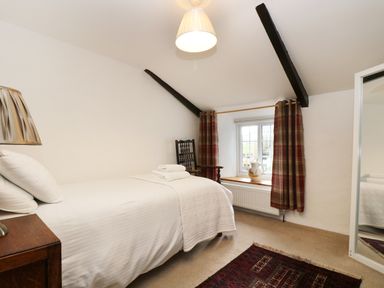 A bedroom with a single bed bedside table chair window with plaid curtains and a rug on the floor at 13 Castle Hill in Lostwithiel