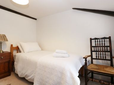 A single bed with white bedding and folded towels a wooden chair and a bedside table with a lamp in a small room at 13 Castle Hill in Lostwithiel