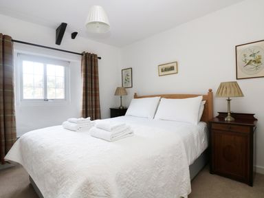 A bedroom with a double bed with white bedding and folded towels bedside tables with lamps and framed pictures on walls at 13 Castle Hill in Lostwithiel