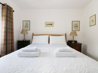 A bed with white linens white towels on top two bedside tables with lamps framed pictures on white walls at 13 Castle Hill in Lostwithiel