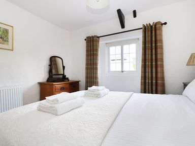 A bedroom with a bed and folded towels on it a wooden dresser with a mirror a window with curtains at 13 Castle Hill in Lostwithiel
