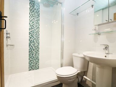 A bathroom with a toilet pedestal sink glass shower enclosure and green tiled shower wall at 13 Castle Hill in Lostwithiel