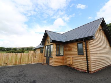 An exterior view of a wooden cabin with a slate roof and a fenced yard at Caban Nant Ddu in Rhayader