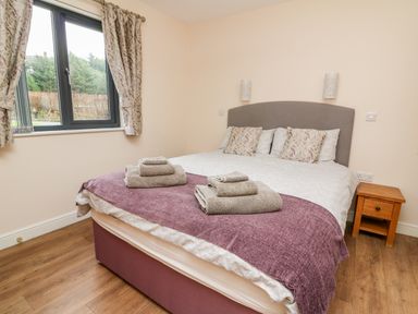 A bedroom with a double bed a purple throw and folded towels on the bed next to a window and wooden bedside table at Caban Nant Ddu in Rhayader