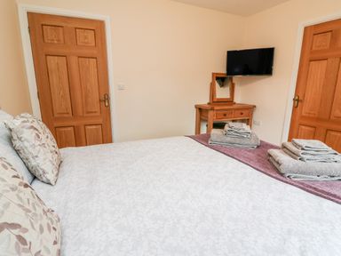 A bedroom with a bed folded towels two wooden doors wooden dressing table with mirror and wall mounted TV at Caban Nant Ddu in Rhayader