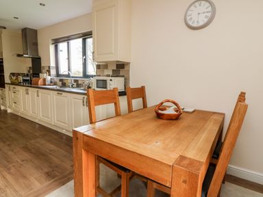 A kitchen with white cabinets a wooden dining table with four chairs and a wall clock at Caban Nant Ddu in Rhayader